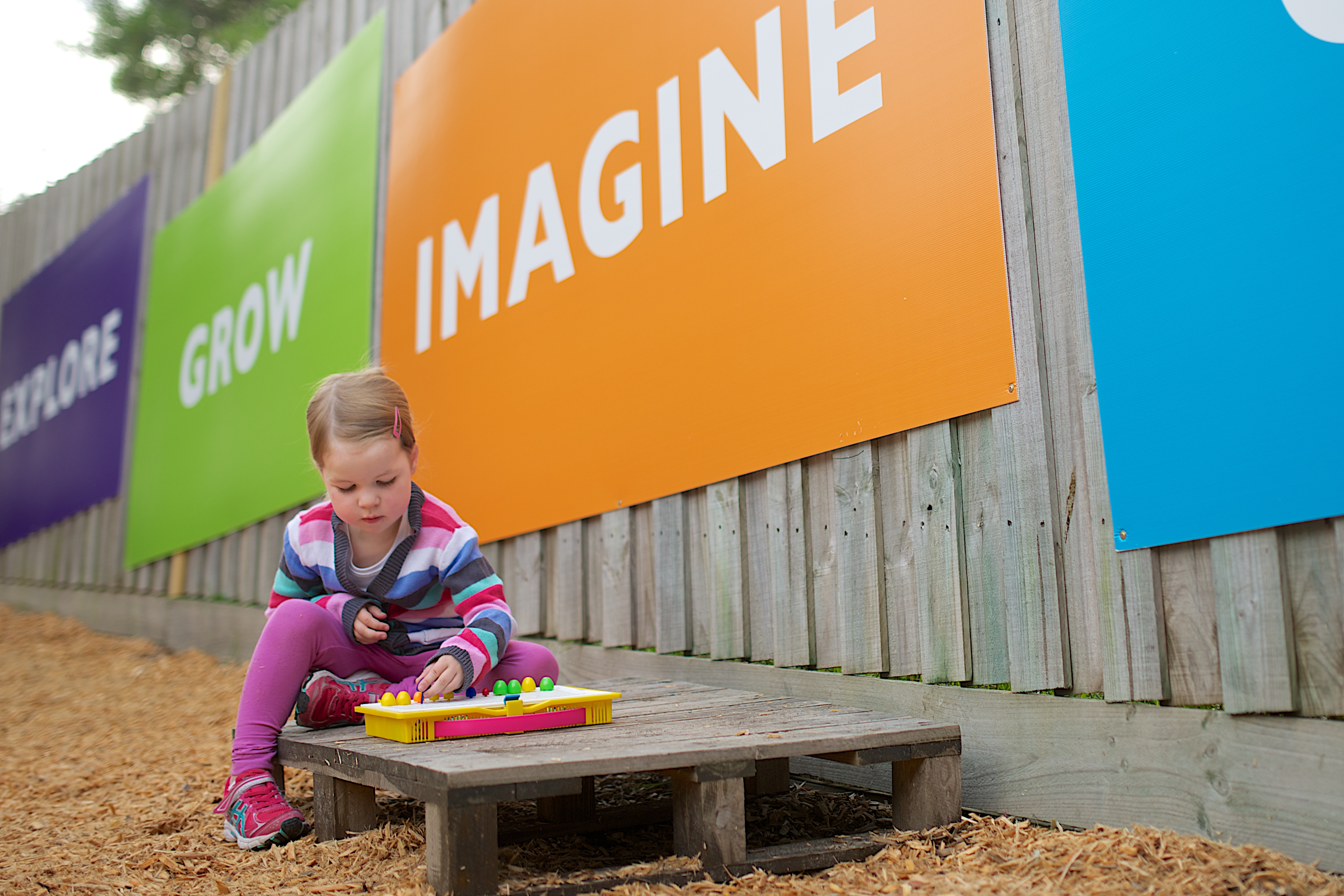 Child playing a board game sitting on a pallet outside