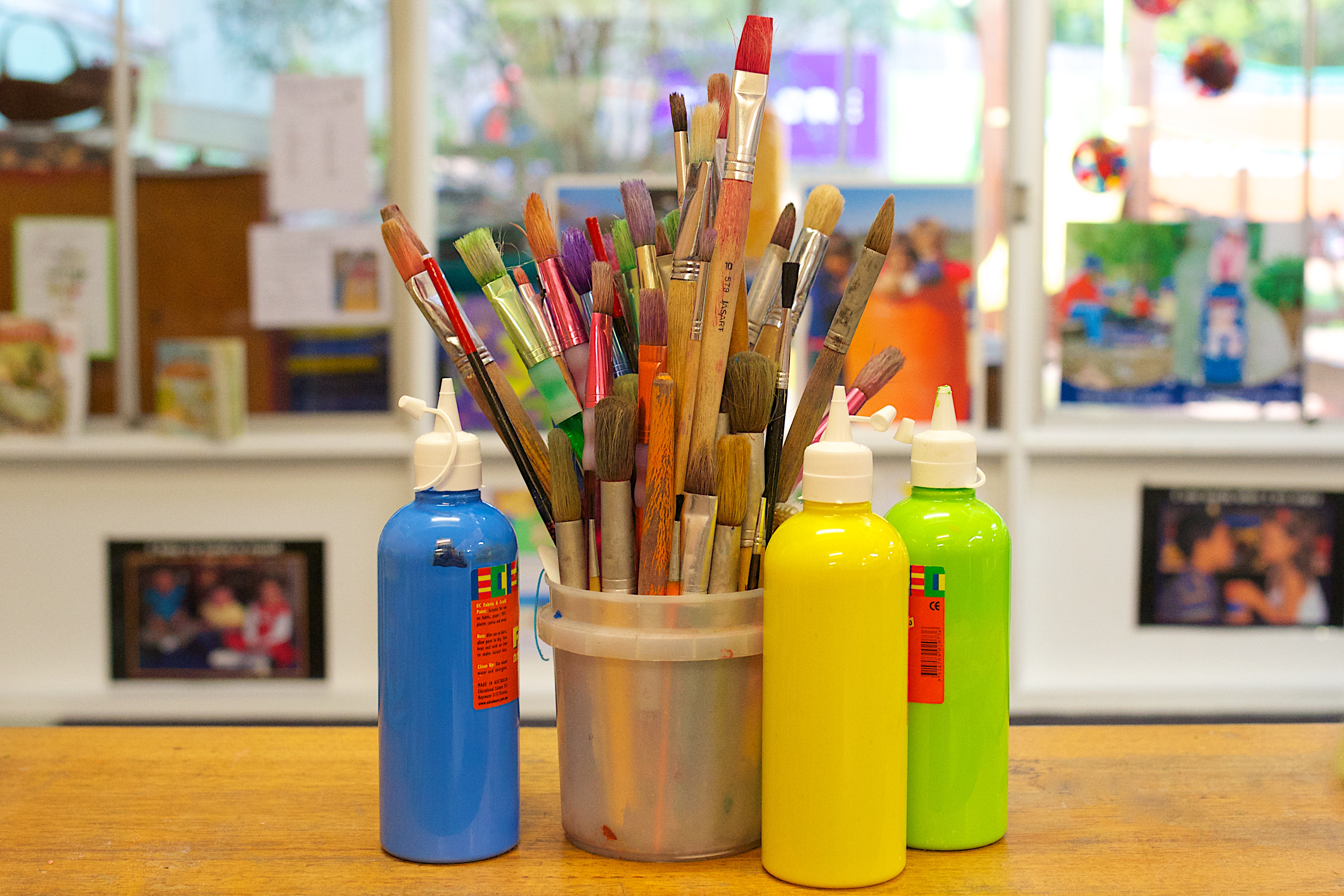 Blue, yellow and green paint bottles around a bucket holding many paintbrushes